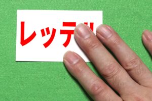 赤い文字で「レッテル」と書かれた紙を人の指が押さえている写真