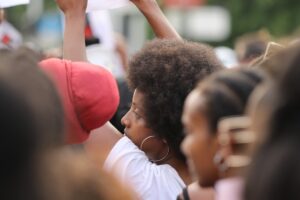 抗議デモで拳を掲げる女性の横顔。民衆の目覚めと怒りを象徴。