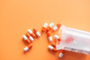 オレンジ色のカプセル薬が容器からこぼれている写真。