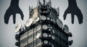 衛星アンテナが密集した通信ビルに、巨大な黒い手が影のように伸びる構図は、国家の通信インフラが国際金融資本に徐々に掌握されていく構造的なリスクを象徴している。NTTの買収と背後の資本関係がもたらす支配構造を視覚化したイメージ。